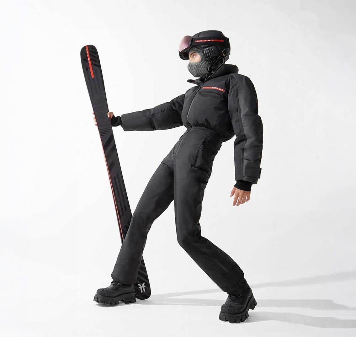Skier dressed in black, skis over the shoulder, studio shot