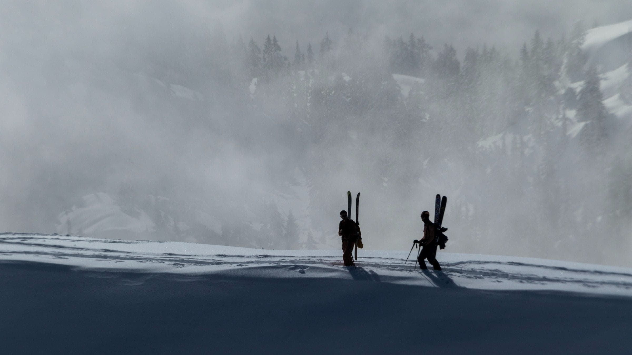 Two ski tourers in silhouette, skis strapped to their packs