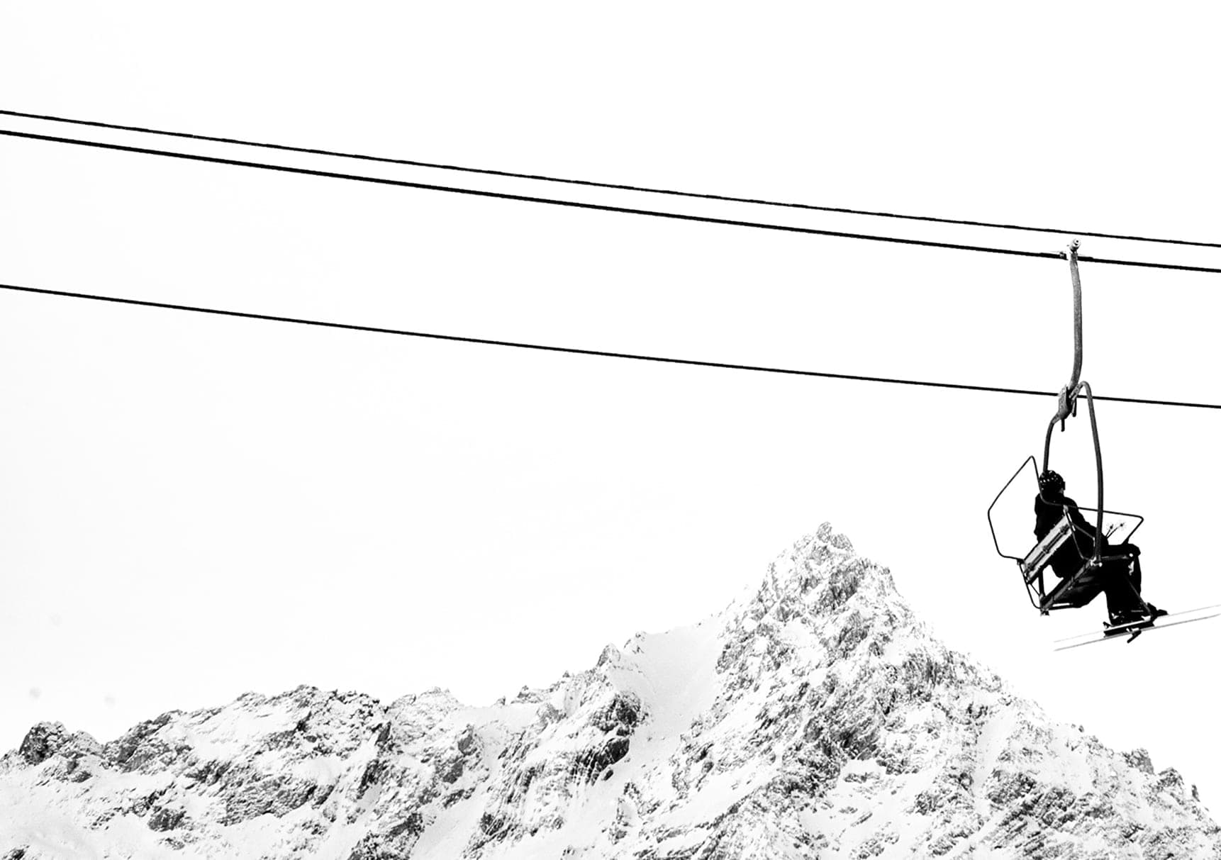 Chairlift with a skier above a steep snow-capped summit, black and white